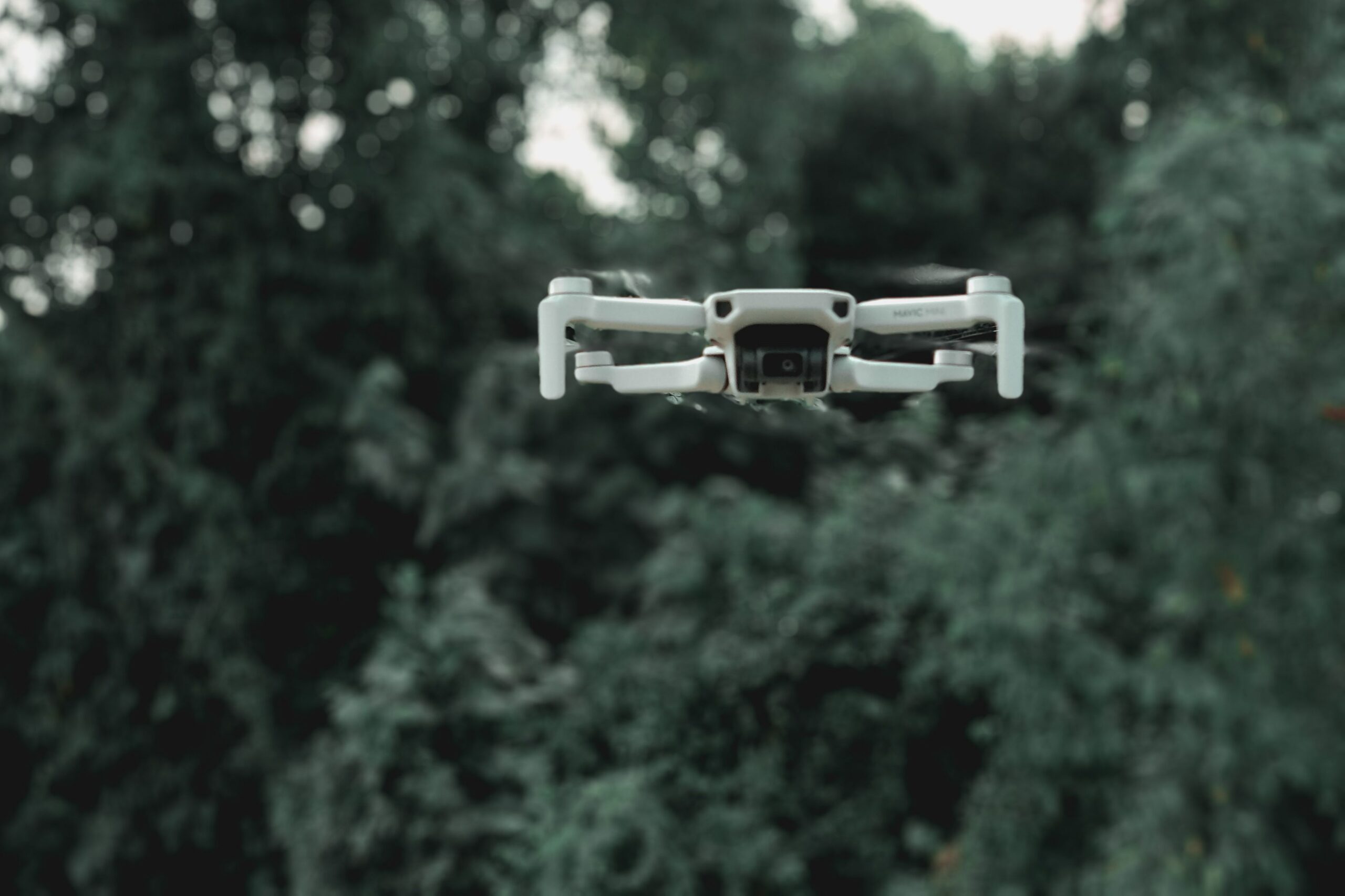 Modern quadcopter with infrared video camera and moving propellers flying under overgrown green trees in daylight